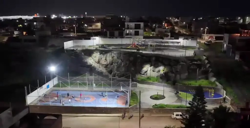 Vista aérea nocturna de un parque deportivo con cancha multiusos, juegos y áreas comunes iluminadas