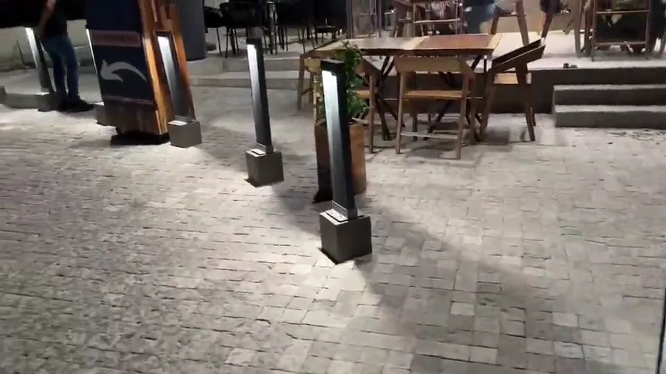 Bolardos luminosos en una plaza comercial con piso de adoquín y jardineras